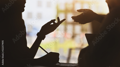 Φωτογραφία silhouette of young designer team standing with a white blank screen laptop and notebook in hands while discussing/talking about them new project with the modern office as background