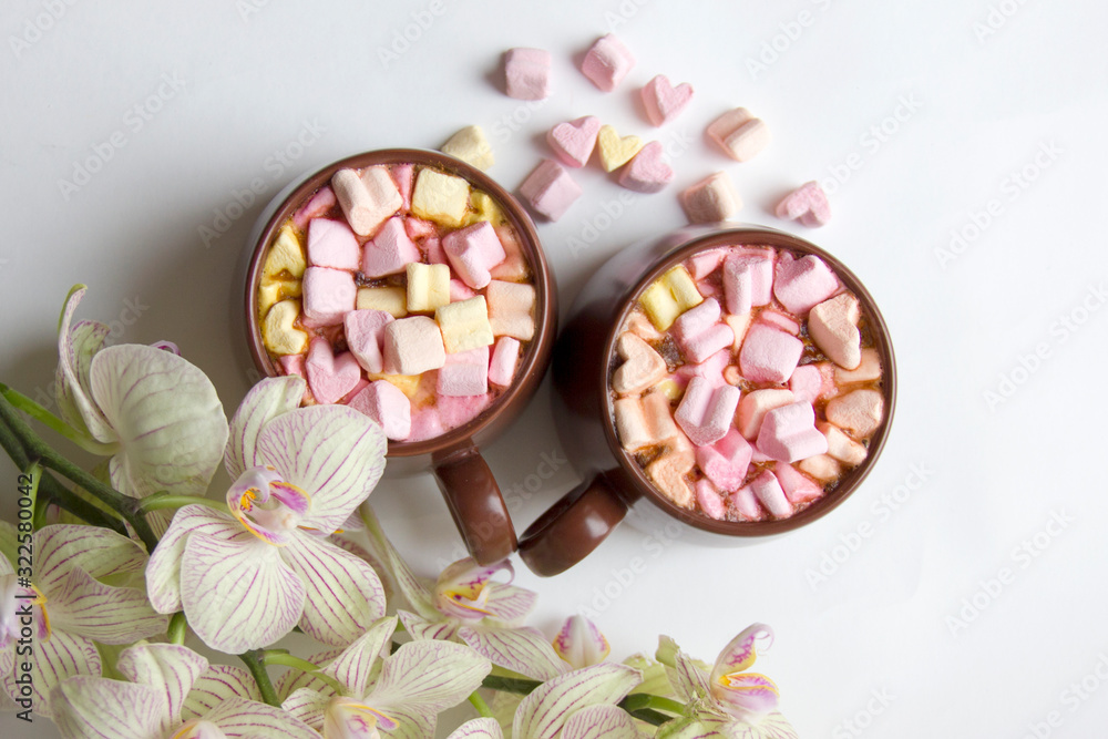 Fototapeta premium Top view of brown cups of hot cocoa with marshmallows in heart shape on white background.