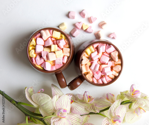 Top view of brown cups of hot cocoa with marshmallows in heart shape on white background.