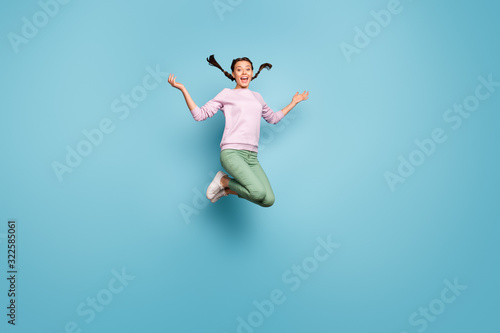 Full body photo of funny lady jumping high good mood throw pretty braids air rejoicing crazy weekend wear casual pink sweater green trousers isolated blue color background