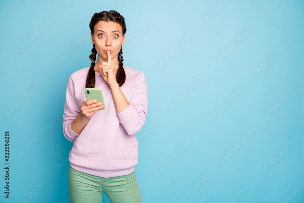 Photo of beautiful lady hold telephone finger on lips reading secret information want to hide it from people wear casual pink sweater green pants isolated blue color background Photo of beautiful lady hold telephone finger on lips reading secret information want to hide it from people wear casual pink sweater green pants isolated blue color background