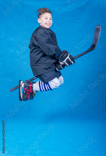 Photography Cheerful young hockey player flying on a hockey stick on a blue background