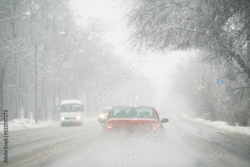 The car is driving on a winter city street in a blizzard