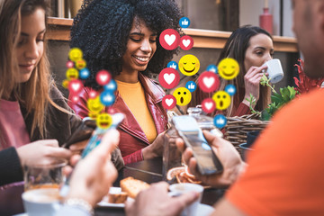 Diverse friends react with social media emoticons while using smartphones in a cafe