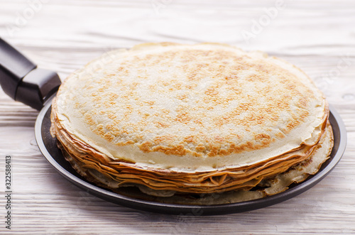 Stack of French crepes in frying pan on wooden kitchen table