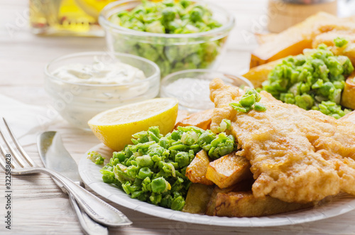 Traditional British street food fish and chips with tartar sauce and mushy peas on paper plate