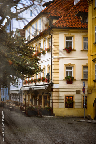 Fototapeta Naklejka Na Ścianę i Meble -  Old yellow house with flowers on windows and restaurant in Praha I, Mala Strana - old district of Prague near Charles bridge. Prague popular tourism travel destination. Sun rays