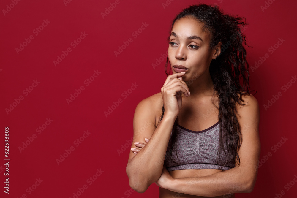 Pensive young african american sports fitness woman in sportswear posing working out isolated on red wall background. Sport exercises healthy lifestyle concept. Put hand prop up on chin looking aside. Pensive young african american sports fitness woman in sportswear posing working out isolated on red wall background. Sport exercises healthy lifestyle concept. Put hand prop up on chin looking aside.