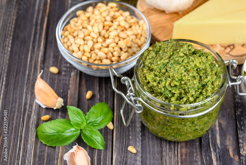 Pesto sauce in a jar with pine nuts, parmesan and garlic over dark wooden background