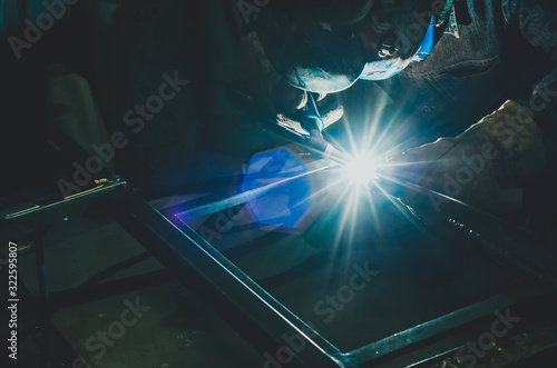 Welding a metal product in metal workshop. Bright glow of an electric arc. Fabrication of metal mounts