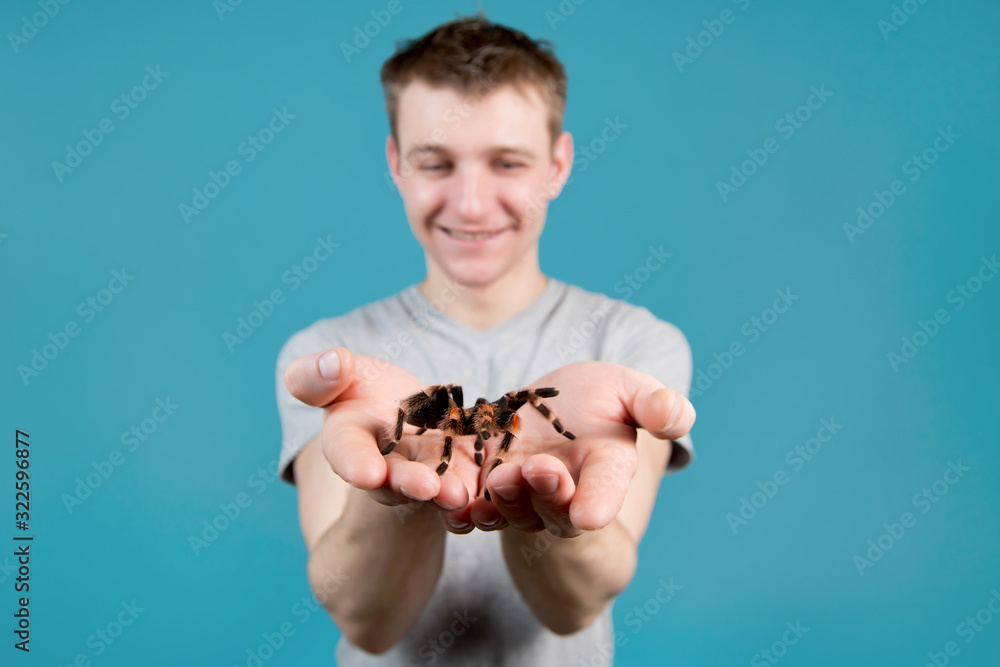 A young man holds a large spider in his arms and holds it to the camera