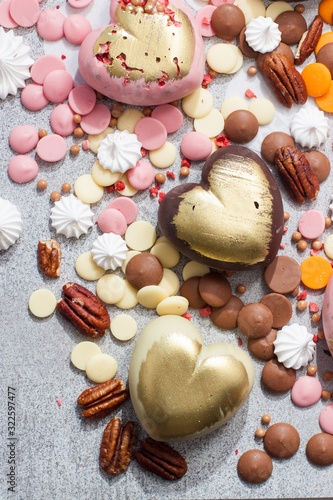 Assorted pink, orange, brown and green chocolate hearts with meringues, pecan nuts and chocolate drops on grey background photo