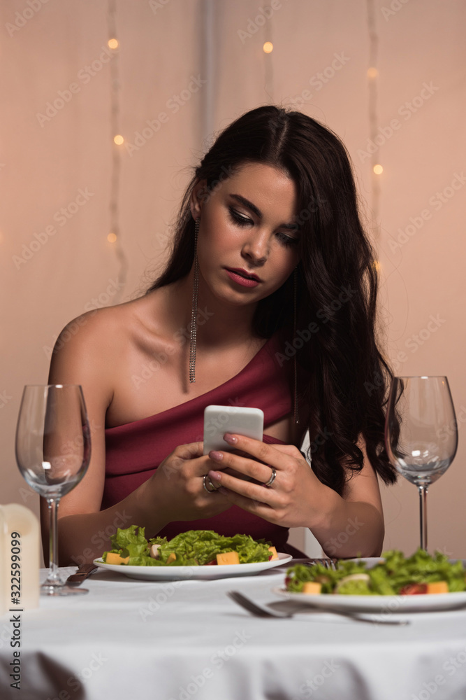 elegant, disappointed girl sitting at served table and using smartphone in restaurant elegant, disappointed girl sitting at served table and using smartphone in restaurant