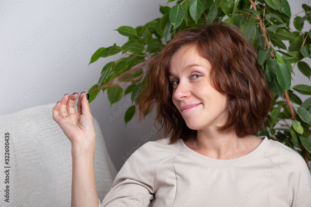 Portrait of a young caucasian brunette girl with curls in a beige dress on a background of a white wall and green leaves of tree. Natural beauty concept, no makeup. Portrait of a young caucasian brunette girl with curls in a beige dress on a background of a white wall and green leaves of tree. Natural beauty concept, no makeup.