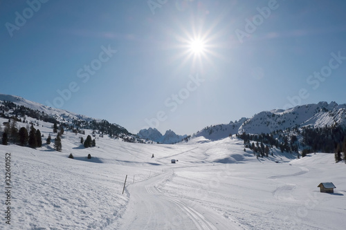 Winter mountain landscape of plateau with forest and snowy old barns. Cross-country ski track winding through hills. Piazza Prato plateau, Sexten Dolomites, South Tyrol, Italy