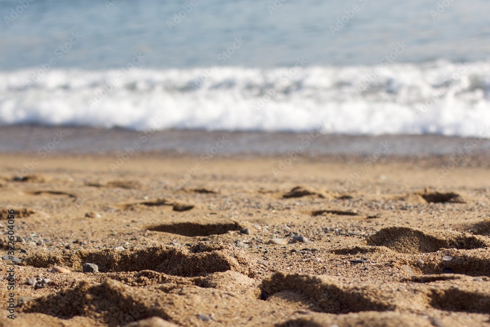 Footsteps in brown sand with waves and ocean in the background Footsteps in brown sand with waves and ocean in the background