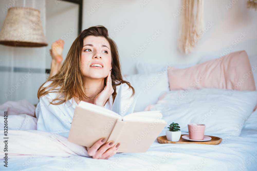 Girl reading a book, drinking coffee or tea, resting in bed. Girl reading a book, drinking coffee or tea, resting in bed.