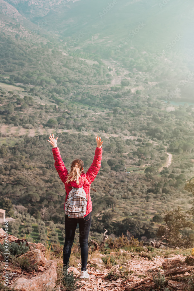 Obraz premium Young woman enjoying view on mountains in sunset, beautiful nature scenery with mountain tops. Girl or woman traveler with backpack alone, woman travelling solo, view from behind, vacation concept