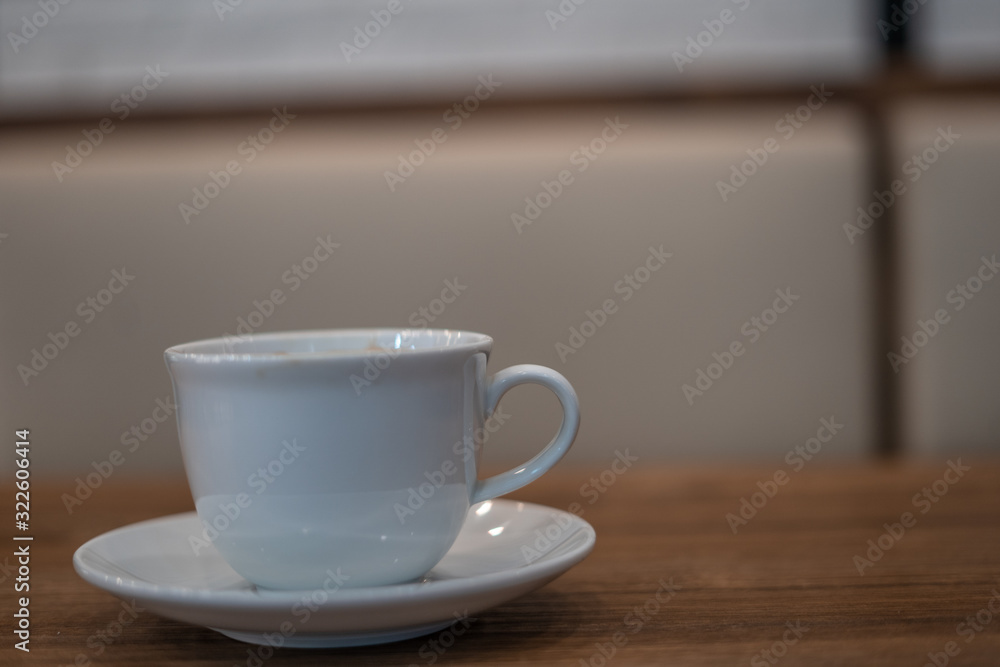 Obraz premium The white ceramic coffee cup with coaster is placed on a brown wooden base on the back, naturally a blurred background.