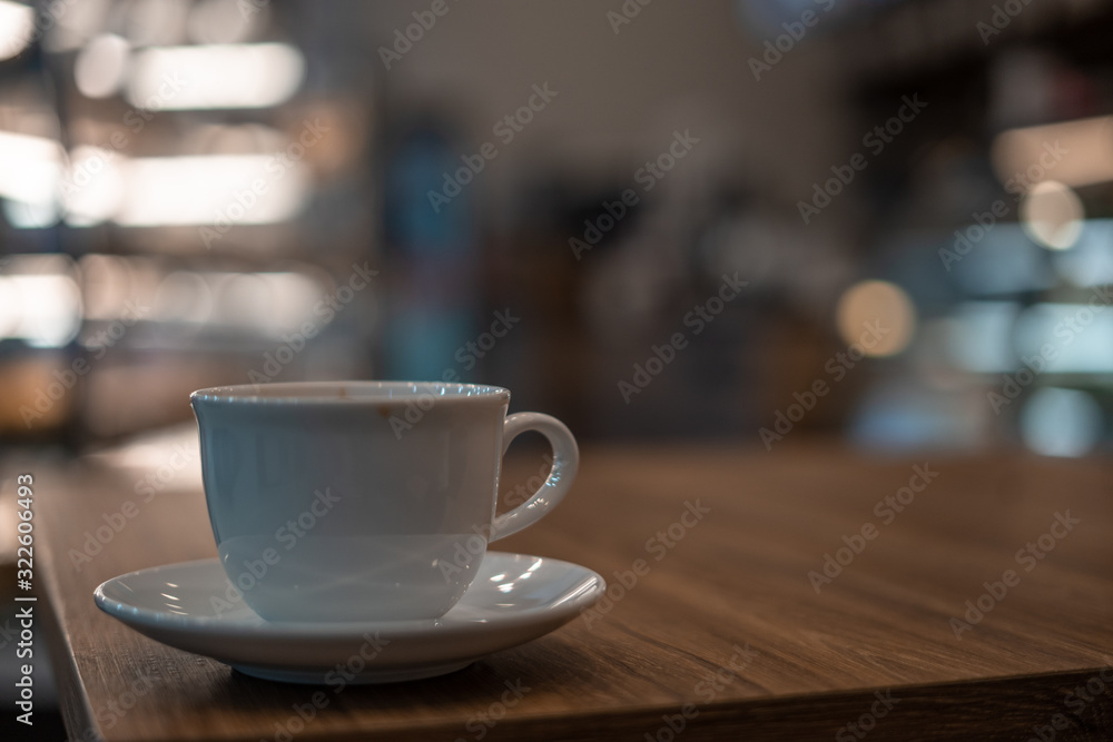	
The white ceramic coffee cup with coaster is placed on a brown wooden base on the back, naturally a blurred background.