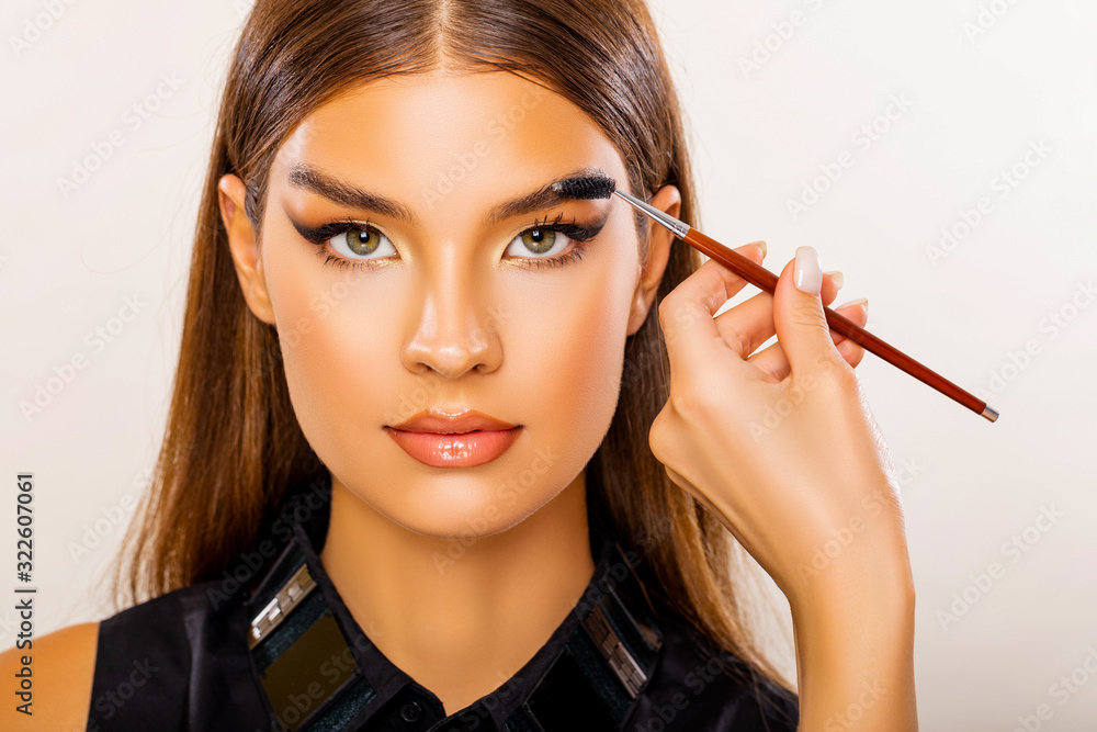 Obraz premium Care beauty eyebrow. Beautiful Young Woman Portrait. Makeup Artist does Face and Eyebrow Makeup. Perfect Bushy Eyebrows. Glossy Peach Lips. Makeup. Beautiful woman with brow brush in hand. 