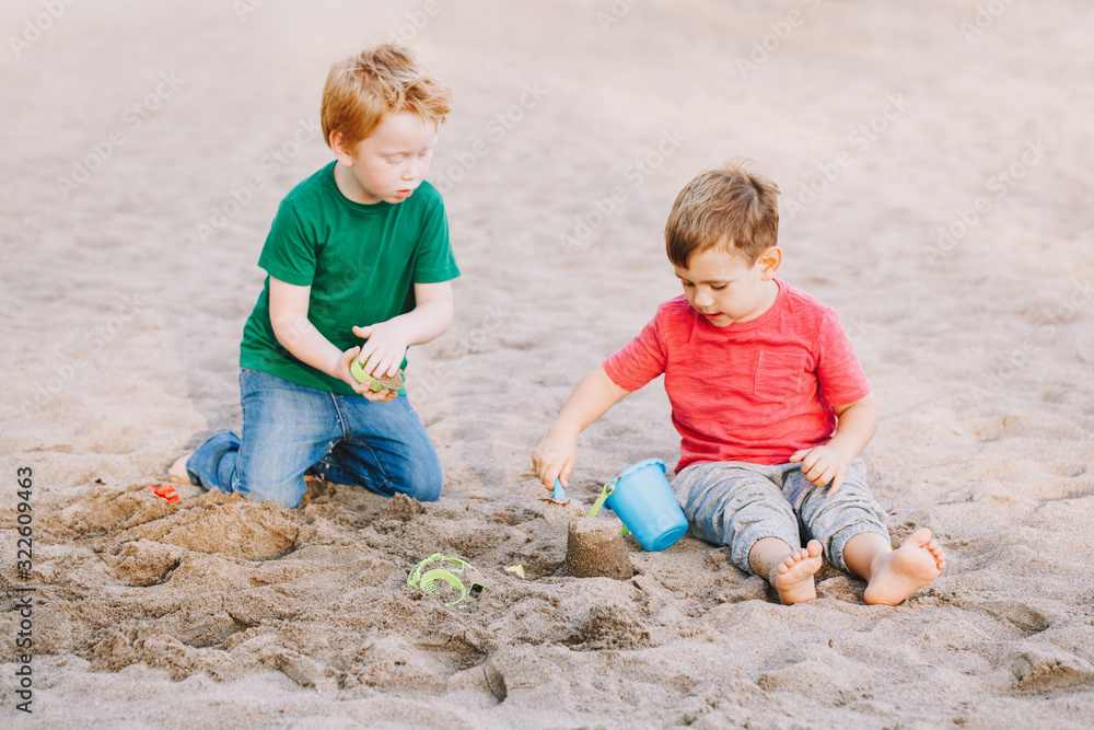 Two Caucasian children sitting in sandbox playing with beach toys. Little boys friends having fun together on playground. Summer outdoors activity for kids. Leisure time lifestyle childhood. Two Caucasian children sitting in sandbox playing with beach toys. Little boys friends having fun together on playground. Summer outdoors activity for kids. Leisure time lifestyle childhood.