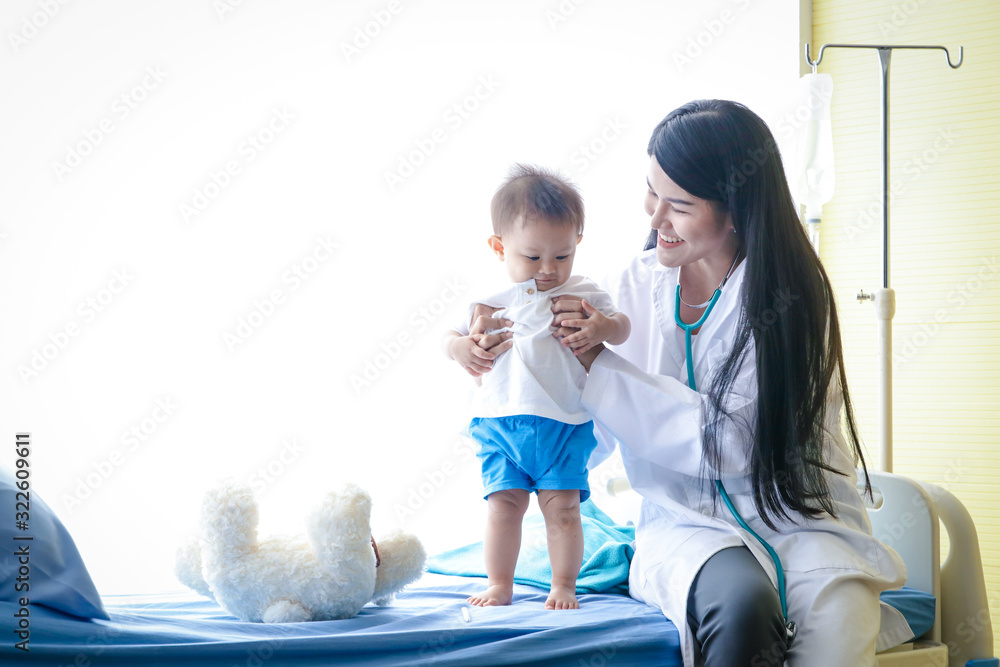Female doctor examines the Asian little boy patient in bed in a clinic. Health care concept Female doctor examines the Asian little boy patient in bed in a clinic. Health care concept