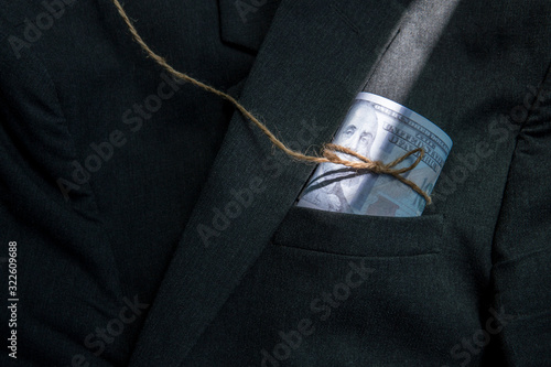 Roll of money dollar tied with rope inside pocket of coat or blazer. Quotes and finance concept.