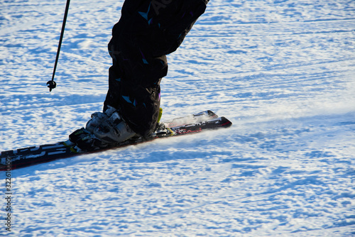 Detail on skis and legs of skier skiing on ski slope