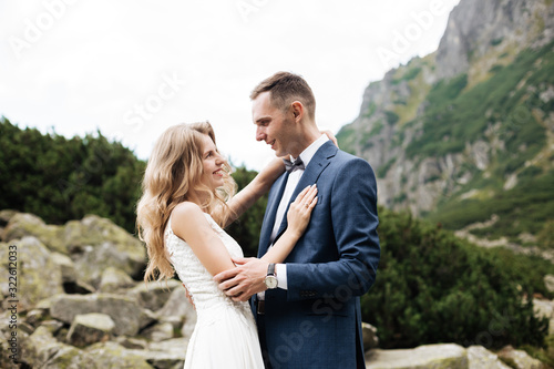 Sensual wedding couple standing on the stony shore of the Sea Eye lake in Poland. © ostap_davydiak