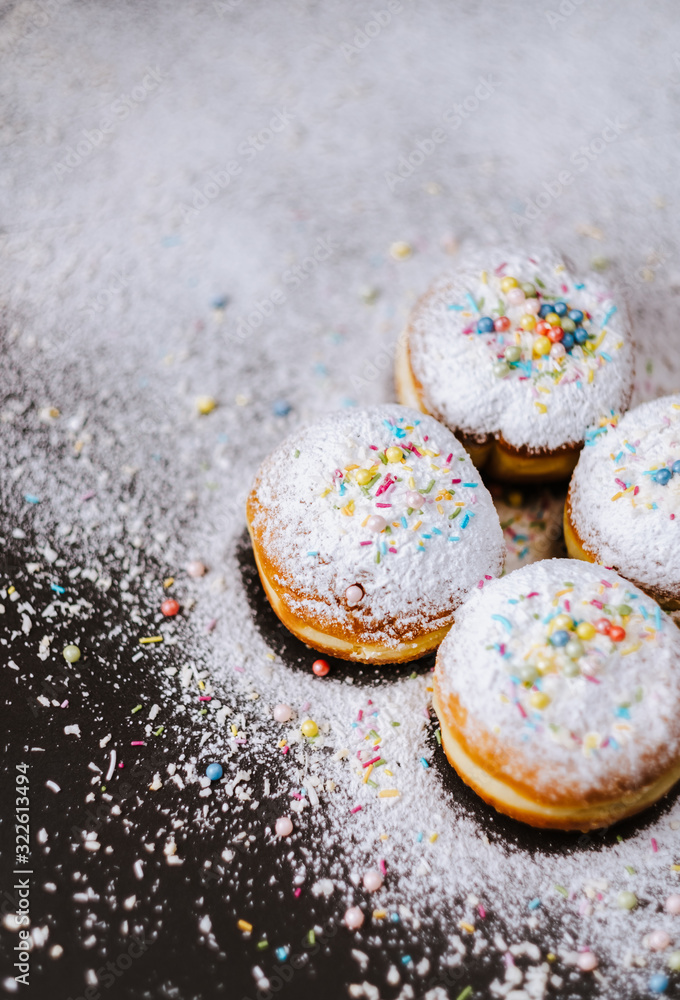 Donuts in powdered sugar and colored sprinkles on a black background. Donuts in powdered sugar and colored sprinkles on a black background.