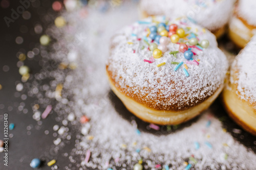 Donuts in powdered sugar and colored sprinkles on a black background. 
