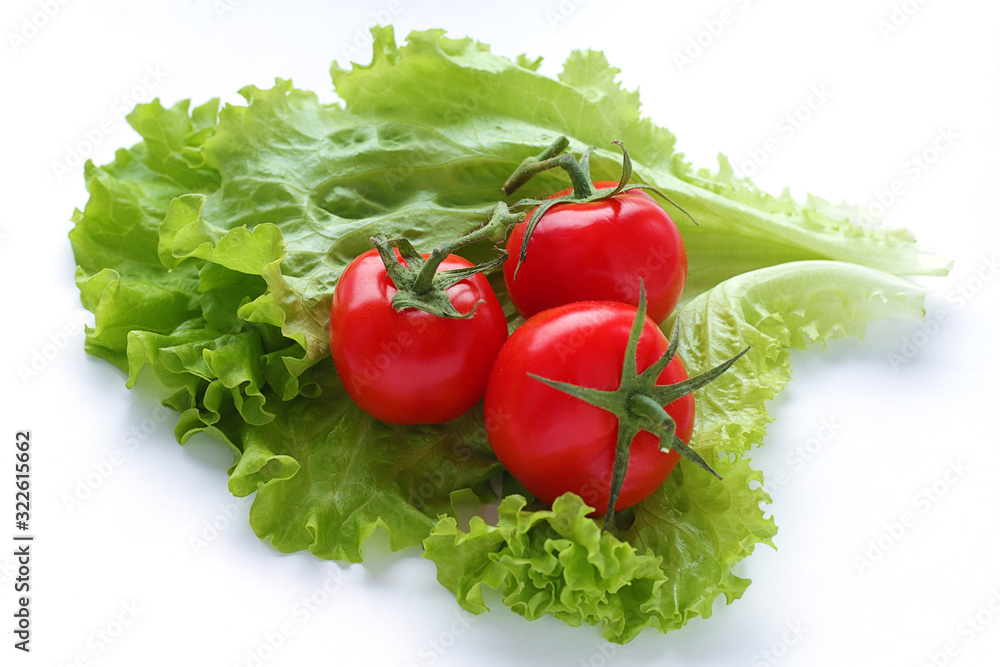 Red fresh tomatoes three pieces and green lettuce leaves lie on a white plain background. Vegetarian diet. Selective focus. Red fresh tomatoes three pieces and green lettuce leaves lie on a white plain background. Vegetarian diet. Selective focus.