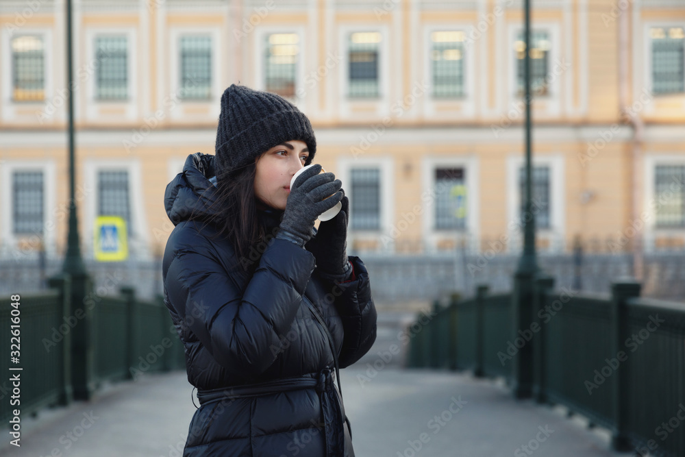 Fototapeta premium A girl with a glass of coffee on the street. Warmly dressed and smiling