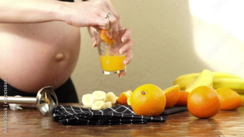 Third trimester pregnant woman prepares some freshly squeezed orange juice to make a healthy fruit smoothie with blender Third trimester pregnant woman prepares some freshly squeezed orange juice to make a healthy fruit smoothie with blender
