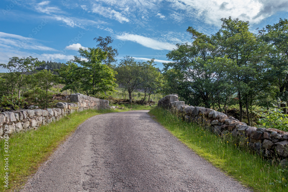 Country road leading over stone wall bridge in Scottish Highlands