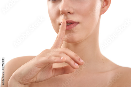 Keep my secret. Beautiful sensual woman keeping finger on lips while standing against white background