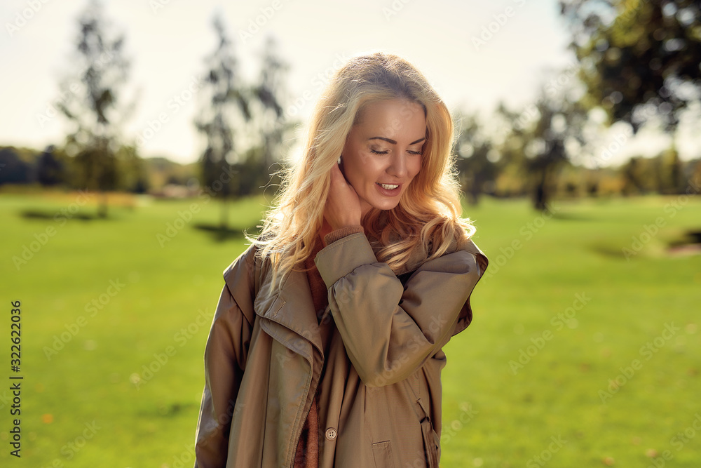 Natural beauty. Portrait of young and attractive woman in beige cloak smiling and enjoying time in the park Natural beauty. Portrait of young and attractive woman in beige cloak smiling and enjoying time in the park