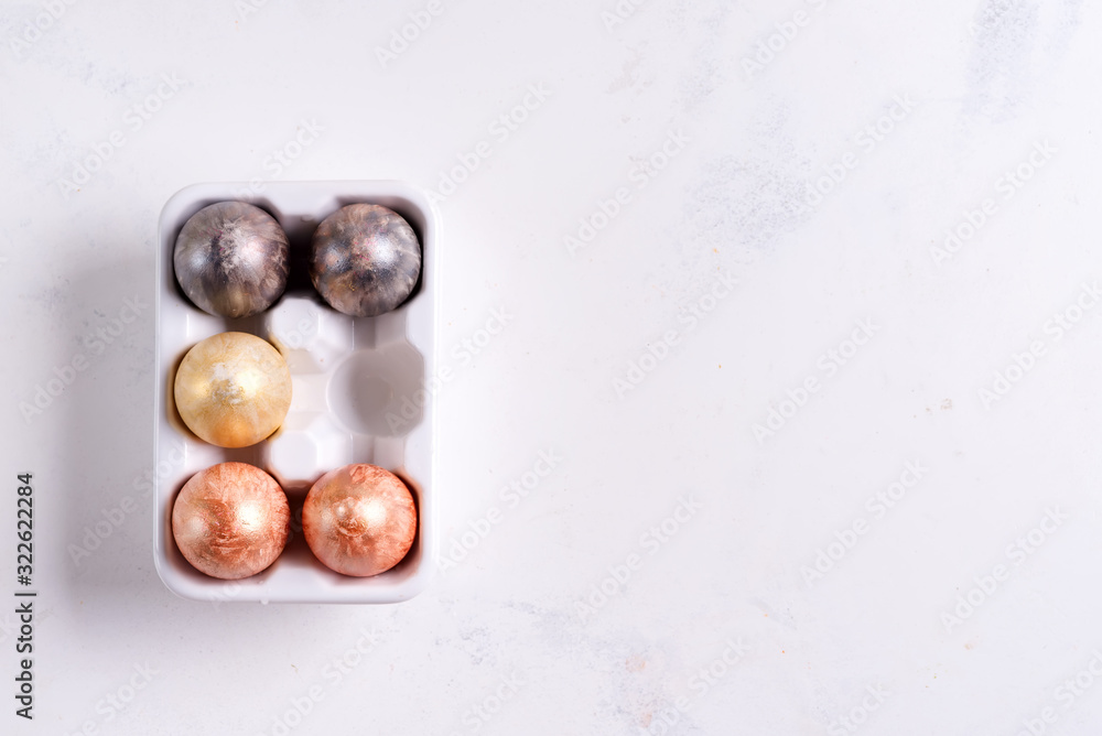 Obraz premium Ceramic egg tray with gold and silver painted Easter eggs on white stone background, holiday concept