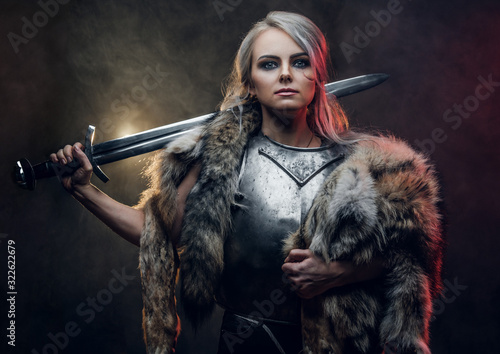 Fotografia Portrait of a beautiful warrior woman holding a sword wearing steel cuirass and fur