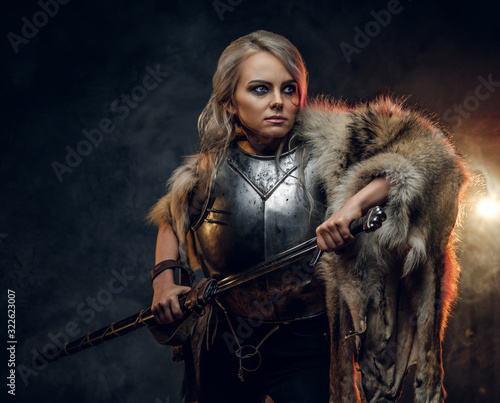 Fantasy woman knight wearing cuirass and fur, holding a sword scabbard ready for a battle. Fantasy fashion. Cosplayer as Ciri from The Witcher.