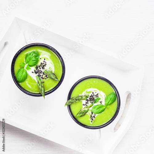 Homemade cream soup with green asparagus, basil and black sesame on white wooden background. Top view, copy space