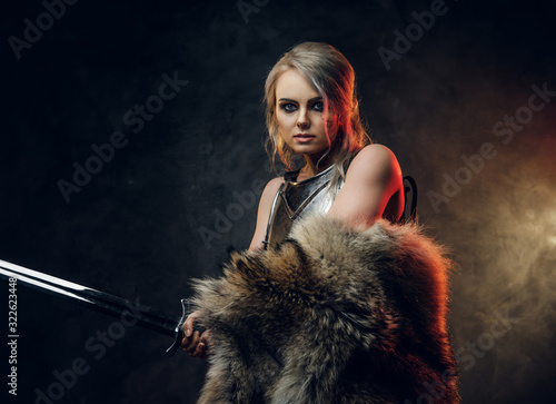 Portrait of a beautiful warrior woman holding a sword wearing steel cuirass and fur. Fantasy fashion. Studio photography on a dark background. Cosplayer as Ciri from The Witcher. photo