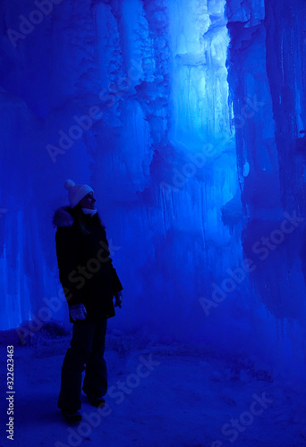 VERTICAL: Young woman exploring an icecave looks at a beautiful ice formation.