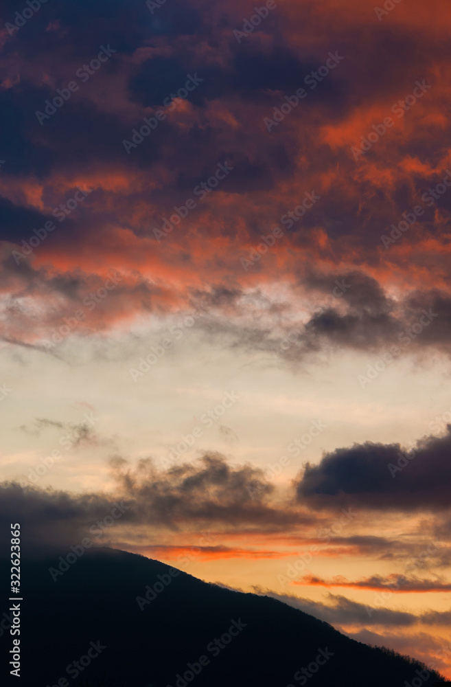 Orange and purple sunset clouds above a mountain as background