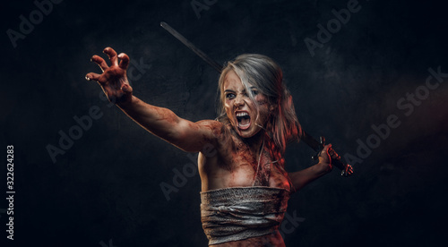 Fantasy woman warrior wearing rag cloth stained with blood and mud holding a sword and rushes into battle with a furious cry. Studio photo on a dark background with smoke. Cosplayer as Ciri from The