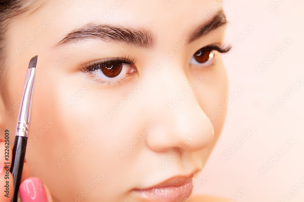 Eyebrow make-up close-up. A young woman is applying makeup on a background.