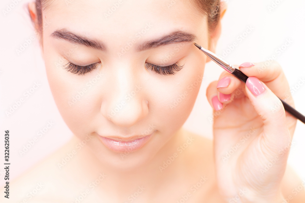 A young woman with a makeup artist is applying makeup. Eyebrow tattoo.