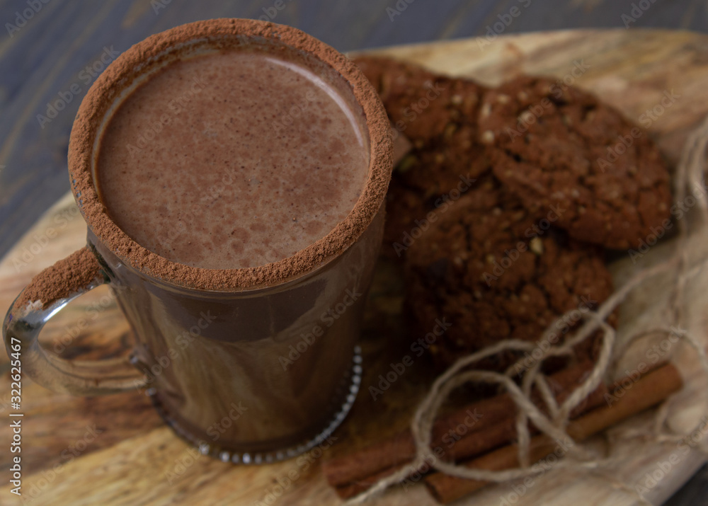 Transparent cup of hot chocolate with cinnamon and milk on a wooden board with oatmeal cookies and chocolate. Transparent cup of hot chocolate with cinnamon and milk on a wooden board with oatmeal cookies and chocolate.