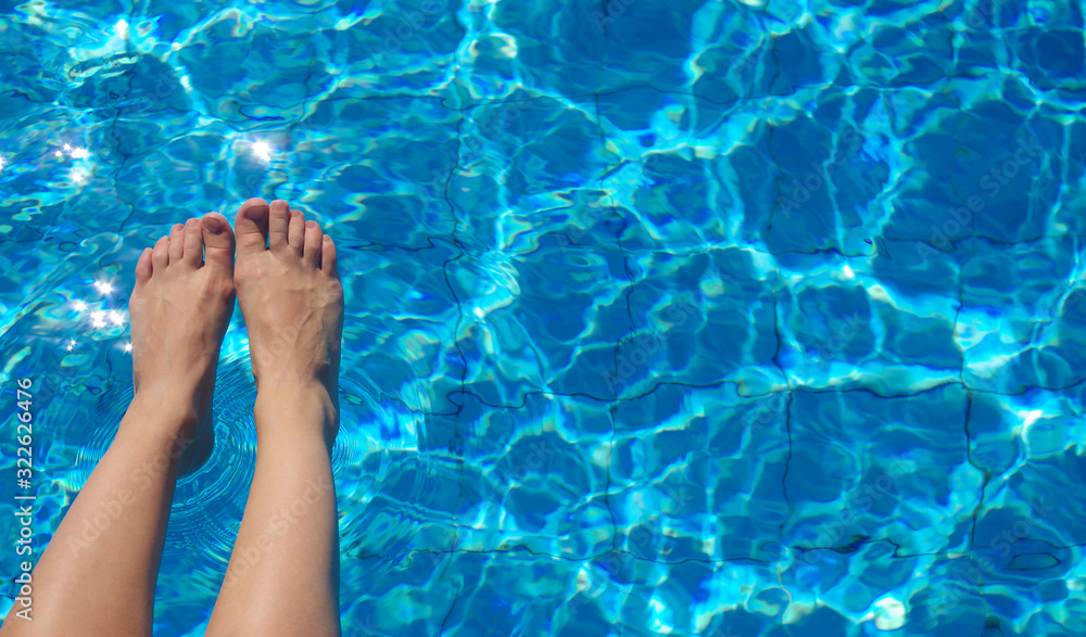 Female legs on the background of the pool. Open space right. Beautiful water texture with sunlight reflections